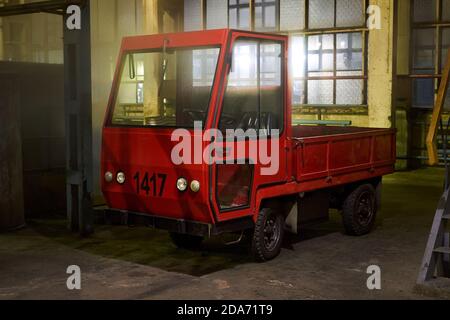 GRODNO, BELARUS - NOVEMBER 2020: Vintage old fashioned style red cargo electric car truck stands into warehouse, late at night at factory or plant. Stock Photo