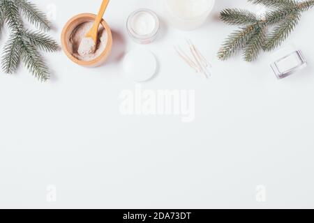 Winter skin care cosmetics and green fir branches on white background with copy space, flat lay. Stock Photo