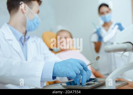 Focus on hands of doctor in protective gloves, mask and white coat takes medical instruments Stock Photo
