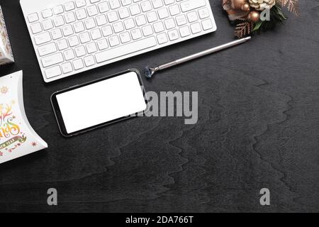 Mockup smartphone with blank white screen, new year gift box with Xmas christmas ornaments on grunge black wood hone office desk background, top view, Stock Photo
