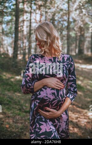 Young pregnant woman holding her belly in a forest. Autumn, summer mood. Stock Photo
