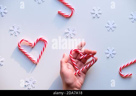 Heart shapes made from candy canes, red white spotted trinkets on white textile. Hand hold heart. Stock Photo