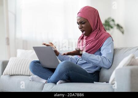 Computer Problems. Angry black muslim lady having troubles with laptop at home Stock Photo