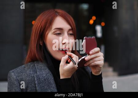 Redhead caucasian business woman looking at little pocket and applying red lipstick work Stock Photo - Alamy