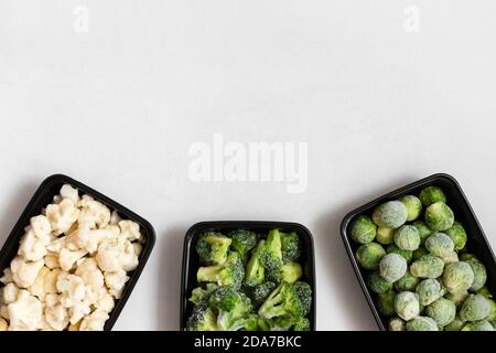 Frame of frozen vegetables in plastic containers on a white background. A set of different cabbages. Space for text. Top view, flat lay. Stock Photo