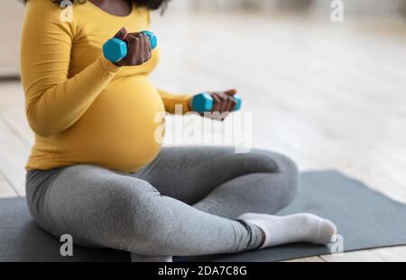 Unrecognizable pregnant woman exercising with dumbbells at home Stock Photo