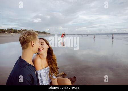 Couple sitting on a dead tree trunk on a beach in Bali at sunset Stock Photo