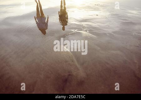 Couple walking on the beach, reflected on the wet sand on a beach in Bali at sunset Stock Photo
