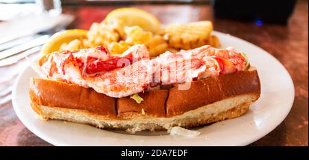 Side view of a lobster roll served with waffle fries on a white plate in a restaurant in Portland Maine. Stock Photo