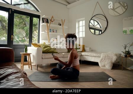 Young african woman using cellphone while sitting on yoga mat at home Stock Photo