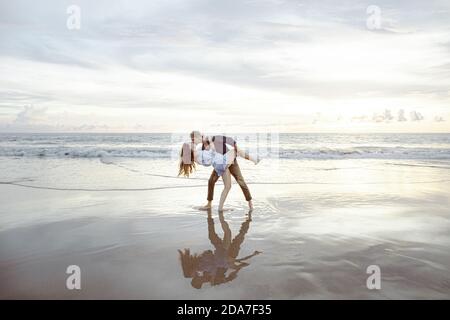 Couple playing and dancing on the beach, laughing and taking a dip. Sunset on a beach in Bali, Indonesia Stock Photo