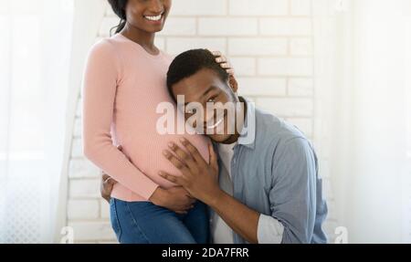 Loving black guy listening his girlfriend's pregnant tummy at home, panorama Stock Photo