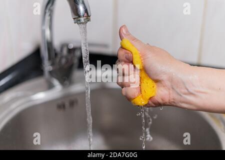 Yellow sponge for dishes under water in girl hand Stock Photo