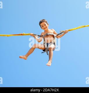 Little boy jumping on a trampoline on blue sky background Stock Photo