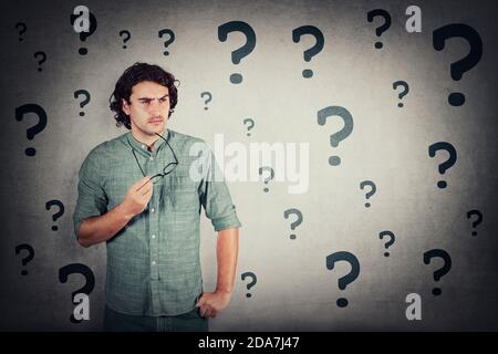 Puzzled man holds eyeglasses in his hand, thoughtful gesture, looking suspicious aside. Confused guy, thinking expression, different interrogation mar Stock Photo