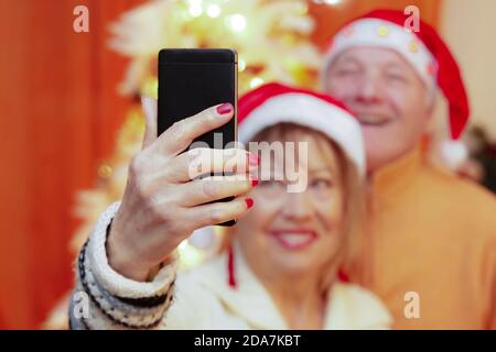 Loving senior couple making selfie on Christmas eve. Focus on hand. Christmas and love concept. Stock Photo
