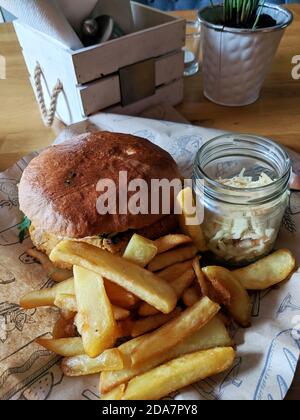 Close up of a fresh burger with french fries and coleslaw salad in a jar on a wrapping paper. Stock Photo