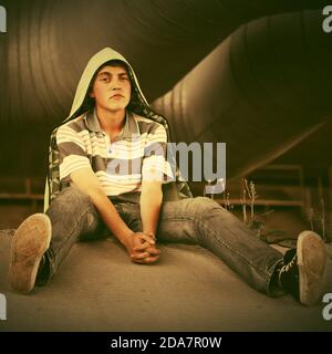 Sad teen boy in depression sitting on the ground Stylish trendy male model wearing light green hoodie and polo shirt Stock Photo