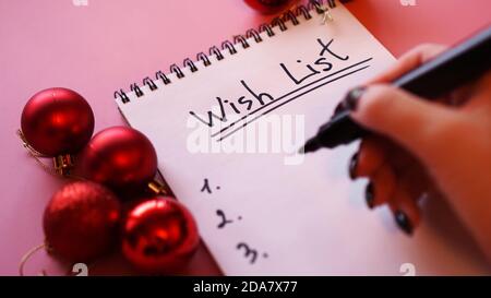 Woman writing her wish list. Festive design on pink background with Christmas red balls Stock Photo