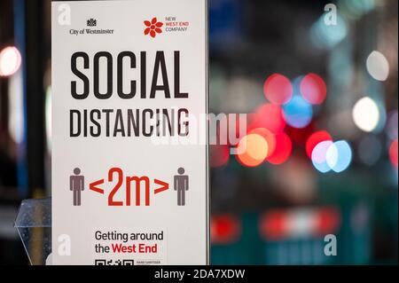 LONDON - NOVEMBER 3, 2020: Social Distancing warning sign with out of focus traffic headlights in the background. Shallow depth of field bokeh effect Stock Photo