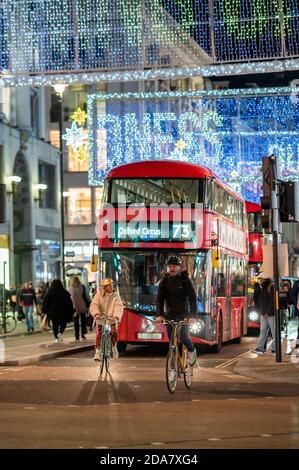 LONDON - NOVEMBER 3, 2020: Cyclists ahead of a Red London Double Decker Bus with Oxford Street illuminated Christmas decorations in the background Stock Photo