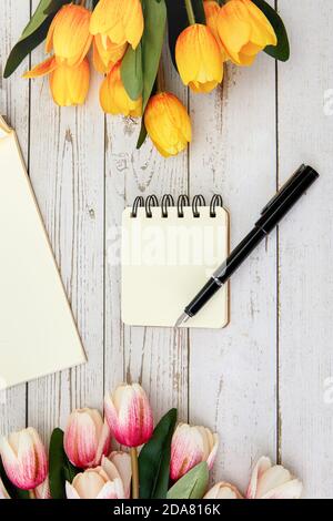 Vertical shot of a blank notebook and a pen, some flowers on a wooden surface Stock Photo