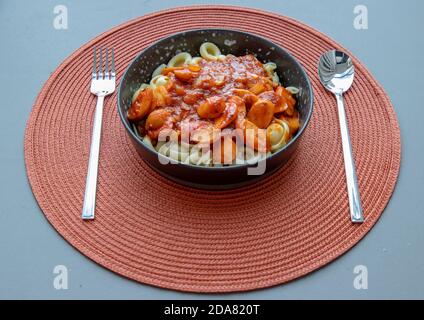 Dischi pasta with sausage, onion and balognese sauce in a black plate on red background. Copy space, No focus, specifically. Stock Photo