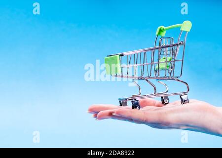 A female hand holds an empty shopping trolley in hand on a blue background. Commercial concept Stock Photo