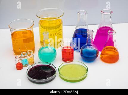 Laboratory glassware with liquids of different colors on white table. Volumetric laboratory glassware over white background. Stock Photo