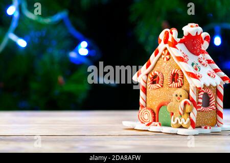 Gingerbread house on a wooden table against the background of a christmas tree Stock Photo