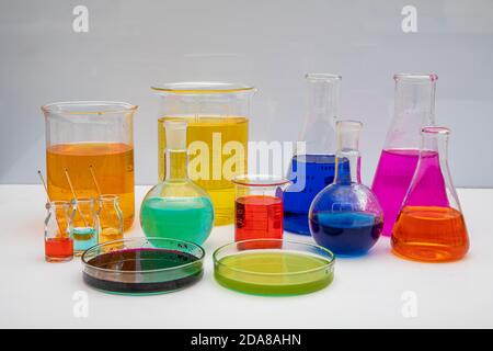 Laboratory glassware with liquids of different colors on white table. Volumetric laboratory glassware over white background. Stock Photo