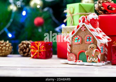 Gingerbread house on a wooden table along with christmas gifts on the background of a christmas tree Stock Photo