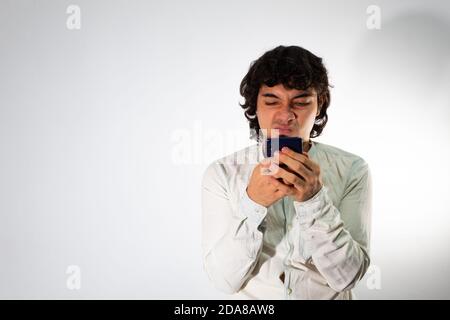 Young hispanic man wearing casual clothes on a white background using a cell phone with angry and worried expression Stock Photo