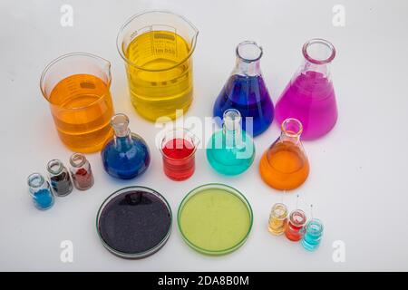 Laboratory glassware with liquids of different colors on white table. Volumetric laboratory glassware over white background. Stock Photo