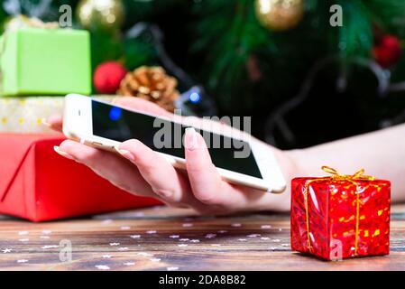 People hand using smartphone for shopping on winter holidays blur Christmas tree background Stock Photo