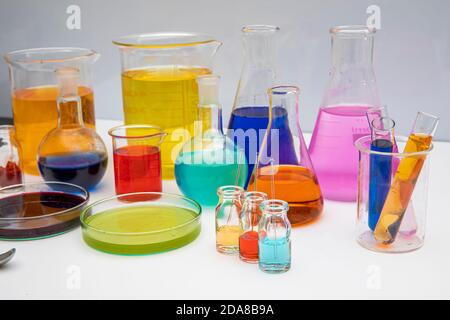 Laboratory glassware with liquids of different colors on white table. Volumetric laboratory glassware over white background. Stock Photo