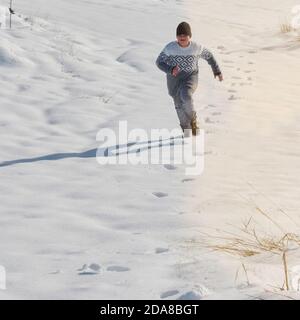 young boy running playing in the snow on a sunny day, happy with the cold Stock Photo