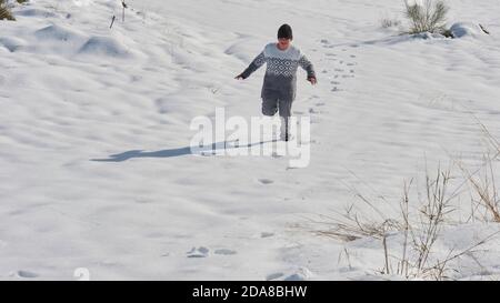 young boy running playing in the snow on a sunny day, happy with the cold Stock Photo