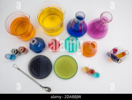 Laboratory glassware with liquids of different colors on white table. Volumetric laboratory glassware over white background. Stock Photo