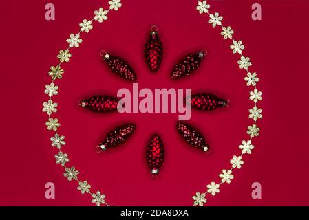 Christmas frame made of red cones and golden snowflakes garland on red background. Christmas decorations with copy space. Stock Photo