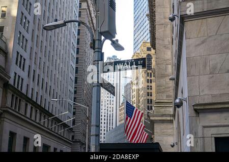 New York City, NY/USA - November 8 2020: Road sign of New York Wall street at the corner Broad street. American flag hanging from the New York Stock E Stock Photo