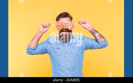 Funny bearded man hold sugar glasses rainbow swirl candy lollipops for birthday party holiday celebration yellow background, fun. Stock Photo