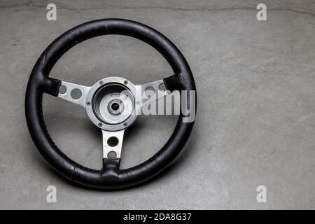 small racing steering wheel with black leather made of aluminum on a polished concrete floor, used steering wheel, a sign for control and management Stock Photo