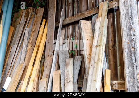 Wooden boards in different sizes and colors leaned against a wall, barn or garage scene with wooden materials. Stock Photo