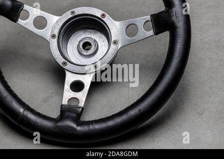 small racing steering wheel with black leather made of aluminum on a polished concrete floor, used steering wheel, a sign for control and management Stock Photo