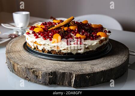 Homemade christmas cake with mascarpone, cinnamon and pomegranate on a wood board on a dining table, cake sideview with surrounding christmas decorati Stock Photo