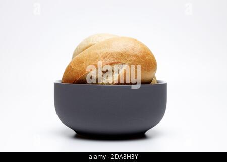 Two typical german wheat buns in a dark grey ceramic bowl on a white uniform background, gold baked buns are typical baked in germany Stock Photo