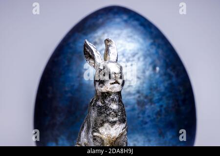 Confident looking easter bunny figure in front of a royal blue easter egg on a white and uniform background, easter decoration ideas Stock Photo