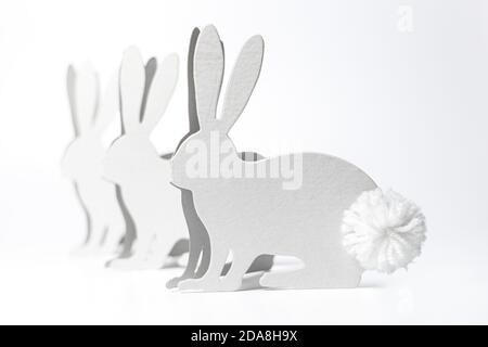 Handmade easter decoration on white background, showing easter bunny silhouettes made from white thick paper, with pompon made of white wool. Stock Photo