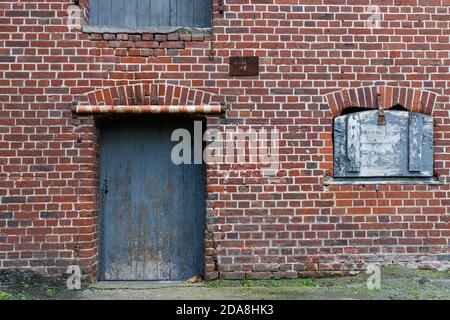 Texture view, a red and weathered brick wall with a blue old door  and a small window with a closed blue painted wooden board. Use as texture referenc Stock Photo